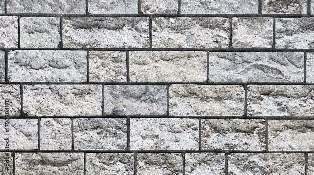 Fototapeta premium Close-up of a gray stone wall made of rectangular blocks with rough, uneven surfaces and visible mortar lines, creating a textured architectural pattern.