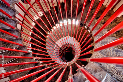 Ljubljana, Slovenia – July 14, 2025: A close-up view of the ornate spiral staircase inside the Ljubljana Castle’s watchtower reveals intricately patterned metal steps and bright red railings.
