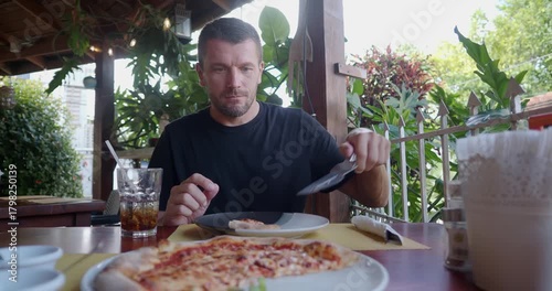 Man enjoying delicious pizza at an outdoor restaurant during a sunny day. 