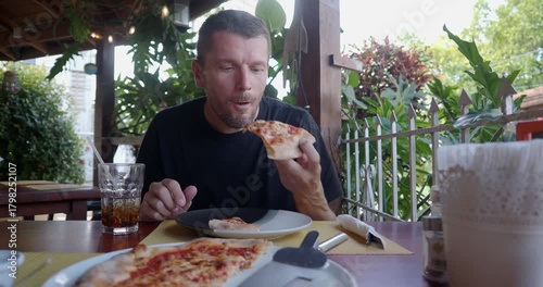 Man enjoying delicious pizza at an outdoor restaurant during a sunny day. 
