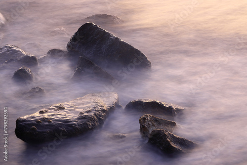 Fototapeta Naklejka Na Ścianę i Meble -  Small rocks in the sea among the waves. The sea has a veil effect with the long exposure technique.