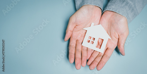 Hands holding paper house cutout, family home security awareness, housing protection idea, financial stability insight, safe shelter symbolism, community support concept