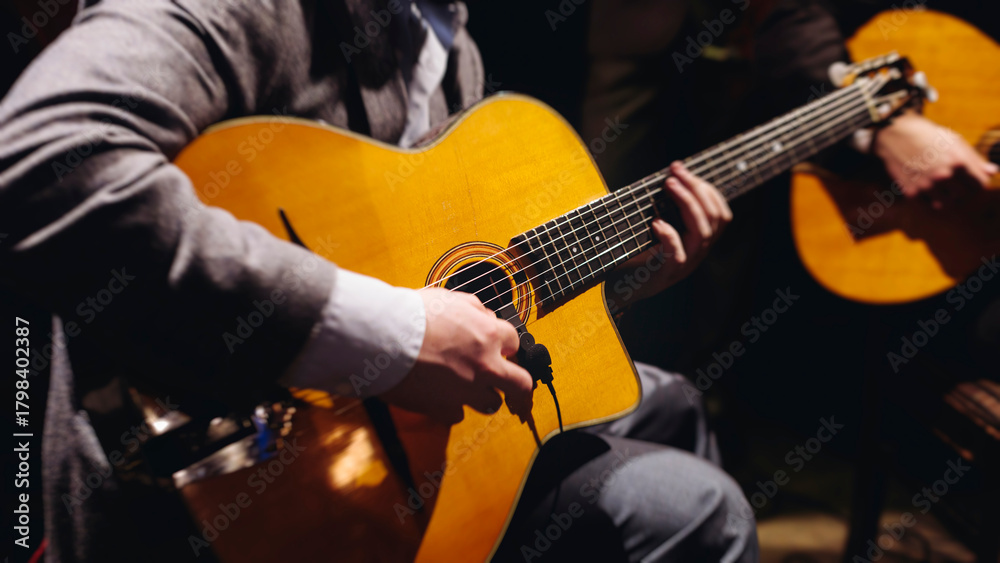Obraz premium Concert view of acoustic electric guitar player with vocalist and rock band performing in a club, male musician guitarist on stage with audience in a crowded concert club hall arena, hands on guitar