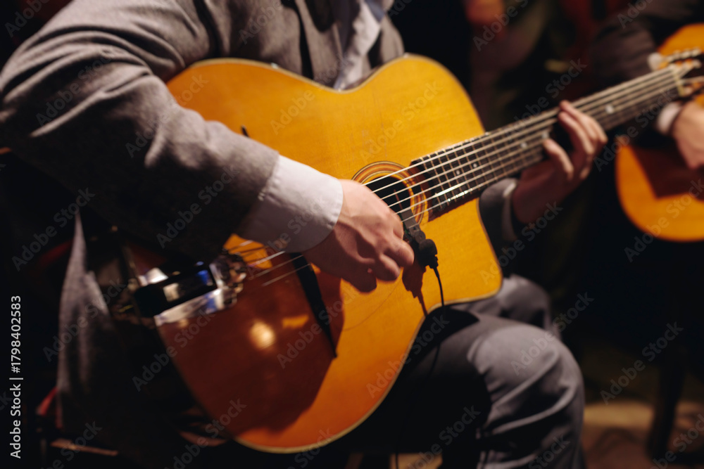 Obraz premium Concert view of acoustic electric guitar player with vocalist and rock band performing in a club, male musician guitarist on stage with audience in a crowded concert club hall arena, hands on guitar