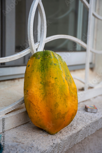 A ripe papaya with yellow and green hues, placed on a windowsill