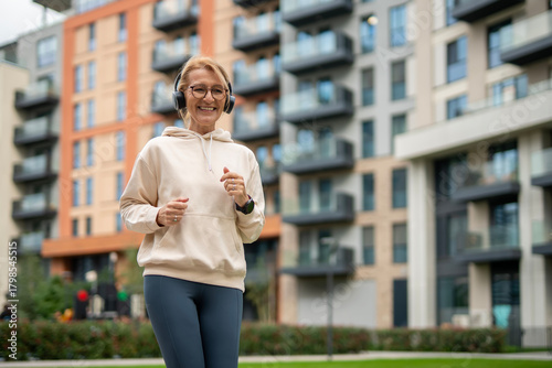 Mature woman jogging happily listening to music in urban park