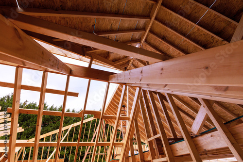 Wooden beams form interior roof truss structure of house being built, revealing work in progress under studs joist