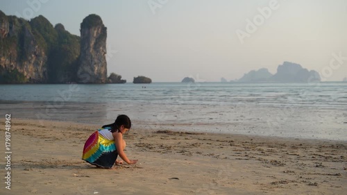 asian child summer or kid girl sitting playing sand on beach or sea on warm sunlight in morning or evening for vacation travel and family holiday relax to people tourists at Krabi Thailand slow motion