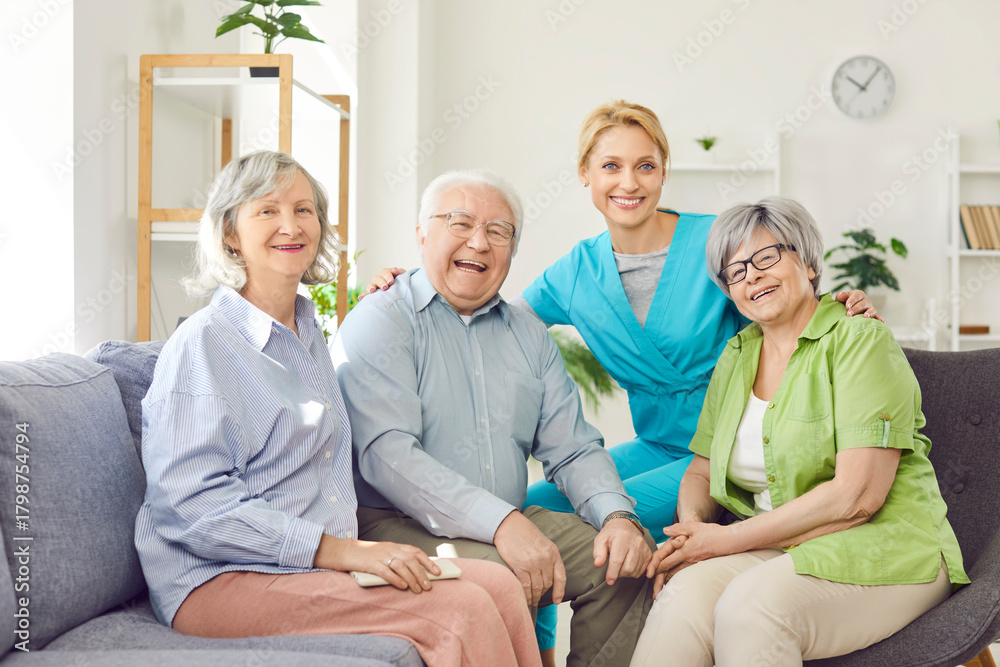 Fototapeta premium Positive group of happy senior people and caring kind smiling nurse, geriatric medicine caretaker providing old help, support during medical visit in retirement home, female doctor caregiving service