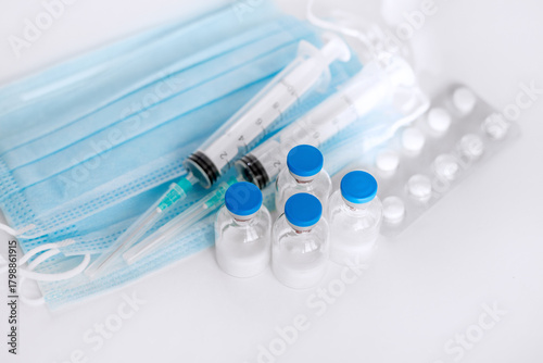 A still life of medical syringes and medication vials. Disposable syringes, medical masks, and fever pills. Supplies for injections and virus protection. 