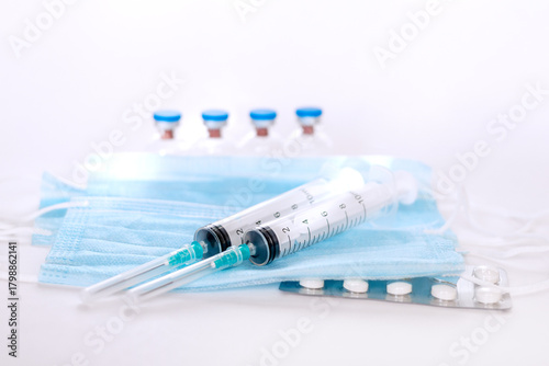 A still life of medical syringes and medication vials. Disposable syringes, medical masks, and fever pills. Supplies for injections and virus protection. 
