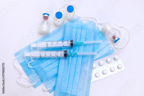 A still life of medical syringes and medication vials. Disposable syringes, medical masks, and fever pills. Supplies for injections and virus protection. 