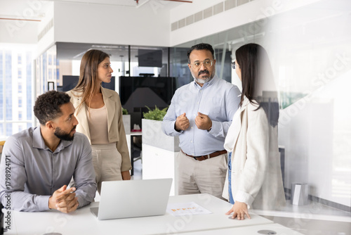 Obraz na płótnie Senior Indian male boss talking to diverse young team briefly