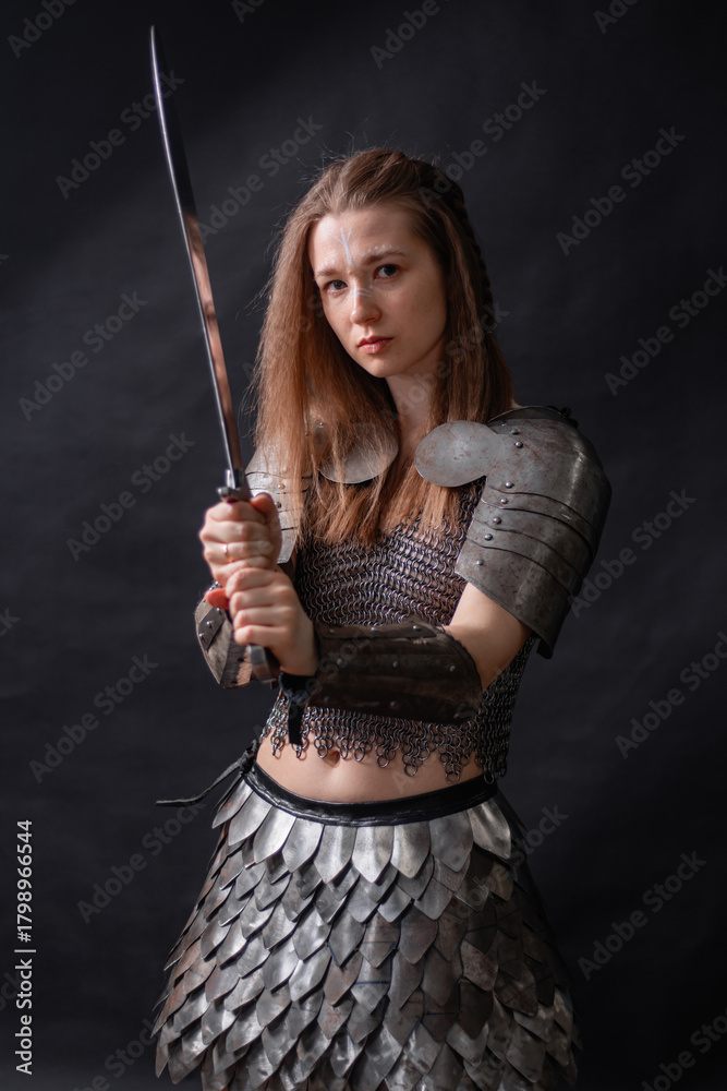 Naklejka premium Portrait of a young woman, fantasy warrior in armor with a sword in her hands isolated on a dark background