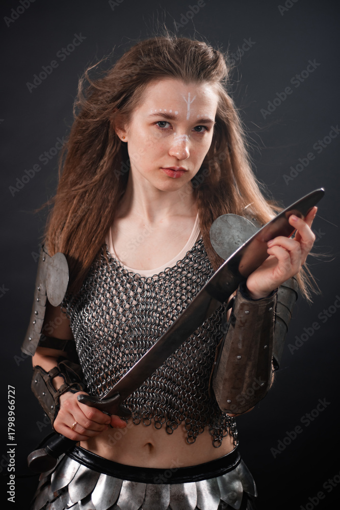 Naklejka premium Portrait of a young woman, fantasy warrior in armor with a sword in her hands isolated on a dark background