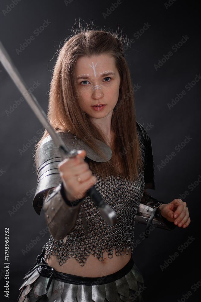 Naklejka premium Portrait of a young woman, fantasy warrior in armor with a sword in her hands isolated on a dark background