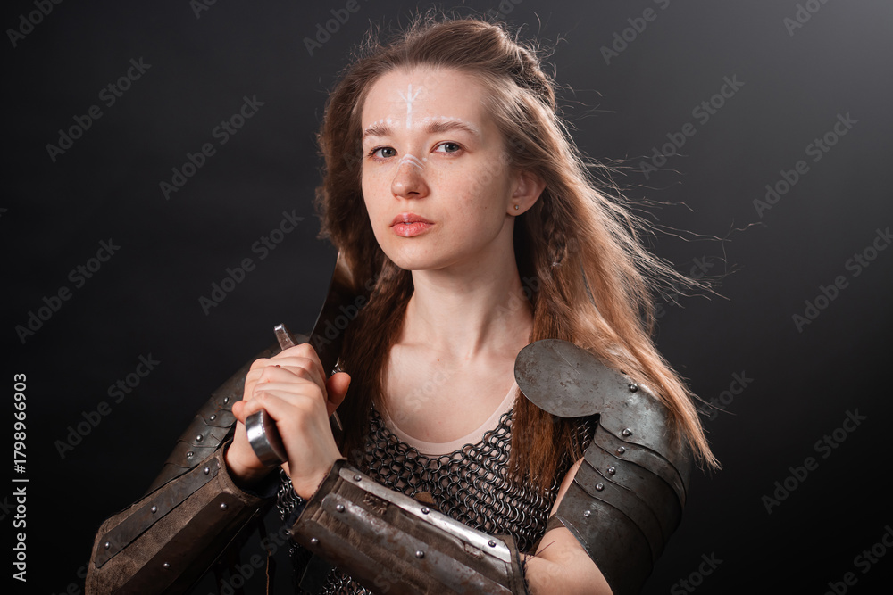 Naklejka premium Portrait of a young woman, fantasy warrior in armor with a sword in her hands isolated on a dark background