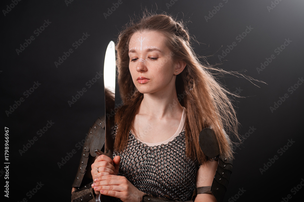 Naklejka premium Portrait of a young woman, fantasy warrior in armor with a sword in her hands isolated on a dark background