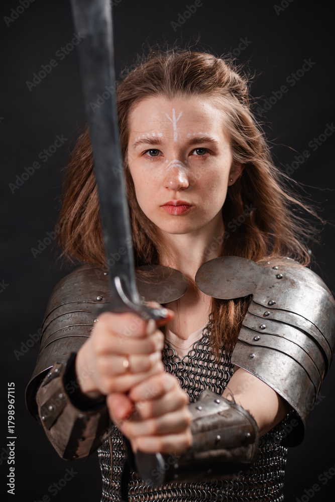 Naklejka premium Portrait of a young woman, fantasy warrior in armor with a sword in her hands isolated on a dark background