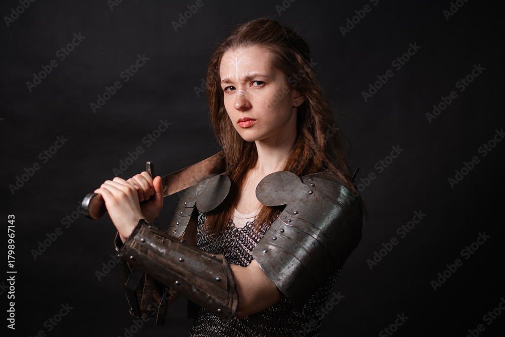 Naklejka premium Portrait of a young woman, fantasy warrior in armor with a sword in her hands isolated on a dark background