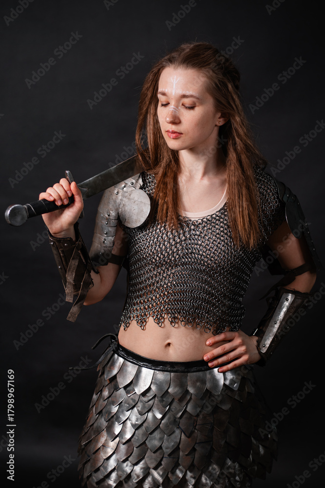 Naklejka premium Portrait of a young woman, fantasy warrior in armor with a sword in her hands isolated on a dark background
