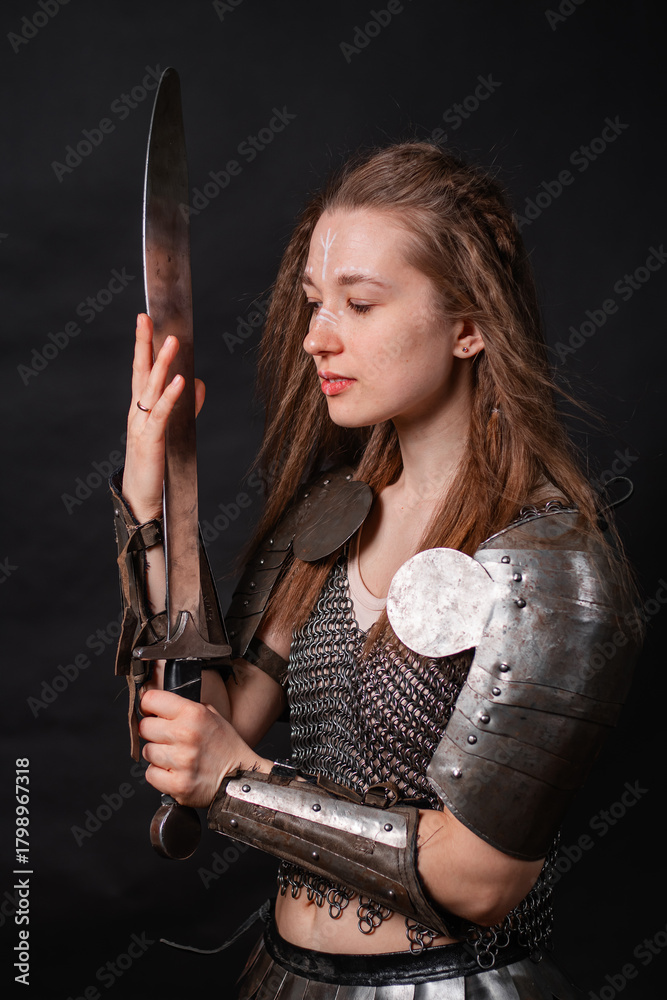 Naklejka premium Portrait of a young woman, fantasy warrior in armor with a sword in her hands isolated on a dark background