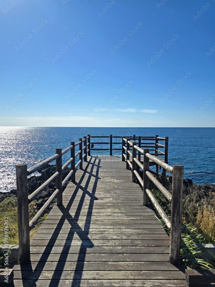 Fototapeta premium A wooden pier leads to the sea, offering a scenic view of the horizon under a clear, bright sky