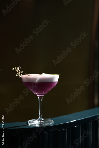 Elegant purple cocktail with foam in a coupe glass on dark background