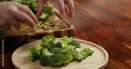 Close-up of hands cutting fresh broccoli on wooden board in kitchen healthy vegan cooking, fresh organic vegetables preparation, clean eating and home cooking concept.