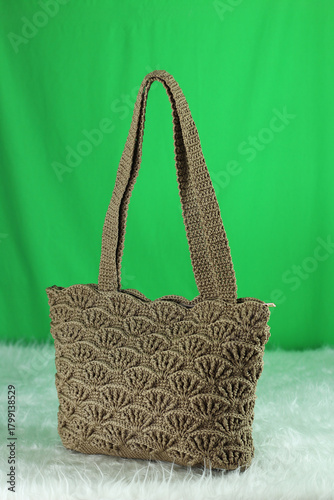 Crocheted  beige bag on a white fluffy blanket in front of a green background.