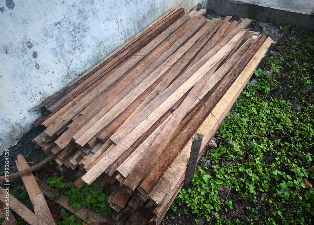 Fototapeta premium Stack of wooden planks outdoors against old wall, raw lumber materials for construction and carpentry work
