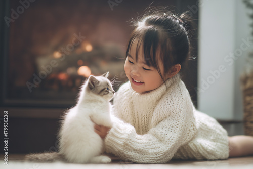 Cute little asian girl hugging her cat in Christmas. Little girl in a white knitted sweater. Holiday concept. Postcard. New Year.