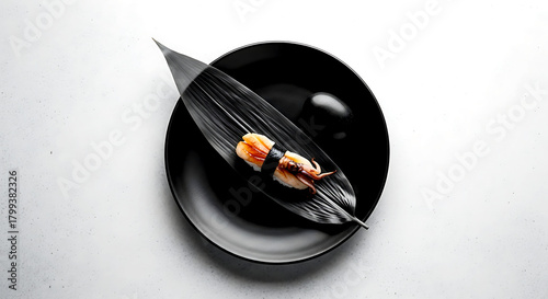 Minimalist flat lay, a monochrome composition a black ceramic plate with a single piece of nigiri with squid (ika), a charcoal-gray bamboo leaf, and a black stone 