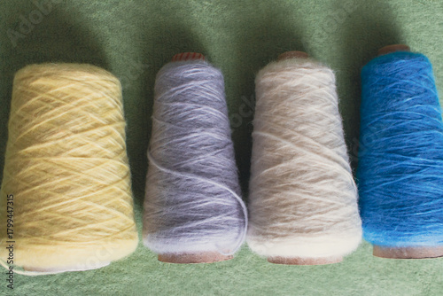Variety colours of alpaca wool and silk. Cones of multicoloured yarn. Wool threads in a row. Row of blue, white, yellow and grey wool. Knitting hobby. Bobbins of yarn. Bright wool for knitting. 