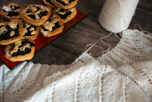 White knitting with beautiful pattern with cakes. Knitting needles and cotton knitting. Beautiful knitted pattern with cotton yarn ball and bakery tart. Knitting hobby. Knitwear concept. Cotton yarn