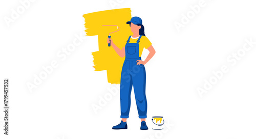Female painter in blue overalls and a cap holding a paint roller and painting a wall yellow.
