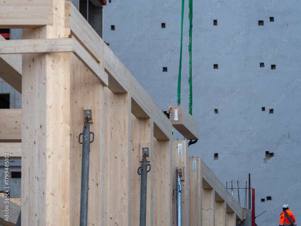 Fototapeta premium Wooden building elements being positioned on a construction site with visible beams and lifting straps