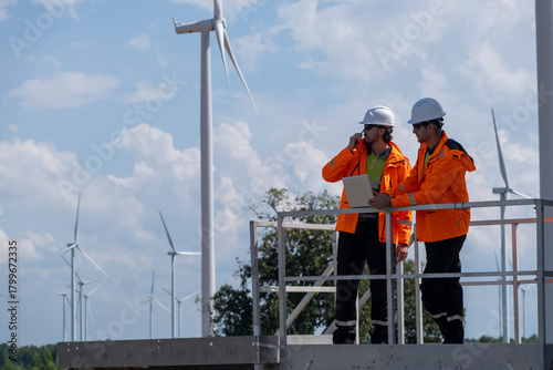 Wind farm technicians inspect equipment and review data at a renewable energy site during a sunny day