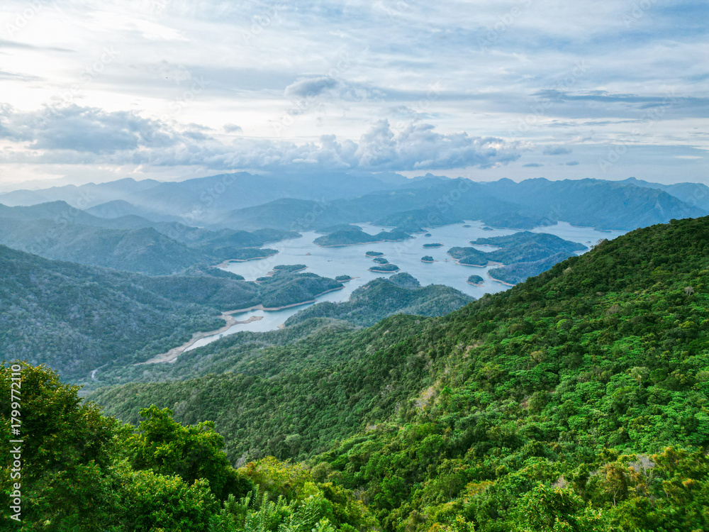 Naklejka premium Scenic aerial view of a lake surrounded by lush green mountains under a cloudy sky