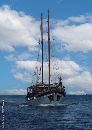 Schooner sailing on ocean under blue sky with clouds