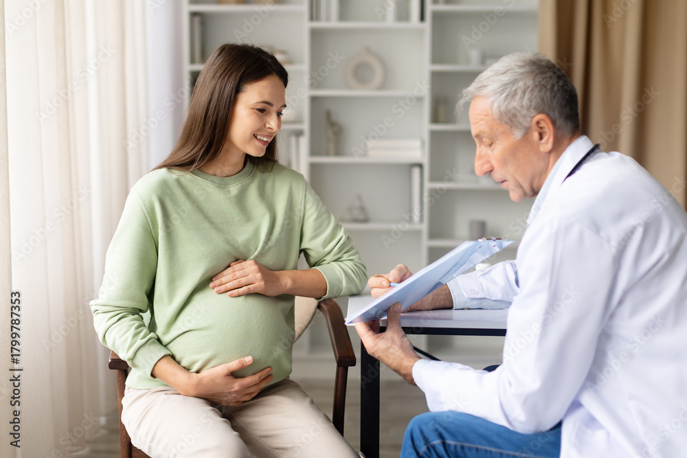 Obraz premium Smiling pregnant woman talking with senior male doctor in clinic during prenatal consultation, maternity healthcare and pregnancy monitoring concept