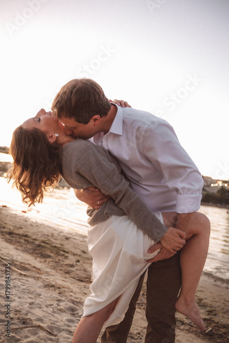 Joyful Couple Embracing on a Beach at Sunset with Warm Light and Urban Waterfront Background