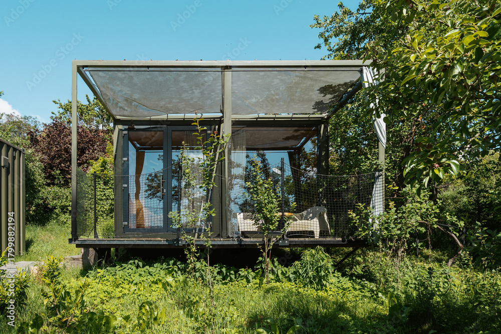 Obraz premium Modern glass cabin nestled in lush green landscape during bright daytime