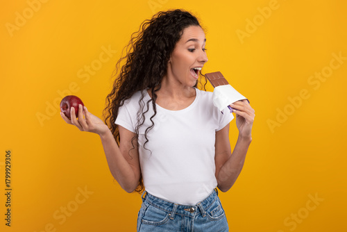 Obraz na plátně Young woman smiles while holding a red apple in one hand and chocolate in the other