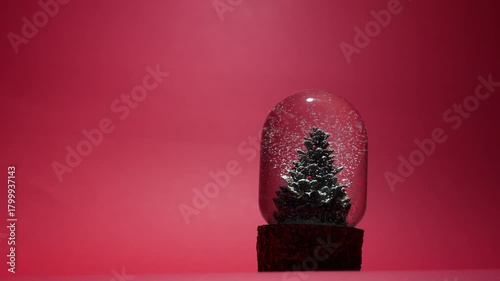 A glass snow globe featuring a miniature Christmas tree inside, with delicate white snowflakes gently falling around it. Festive holiday decoration set in a serene winter atmosphere. 4 k video