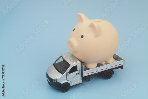 Lorry truck with piggy bank on blue background. Shipping and delivery cost, financial fund relocation and moving money concept.