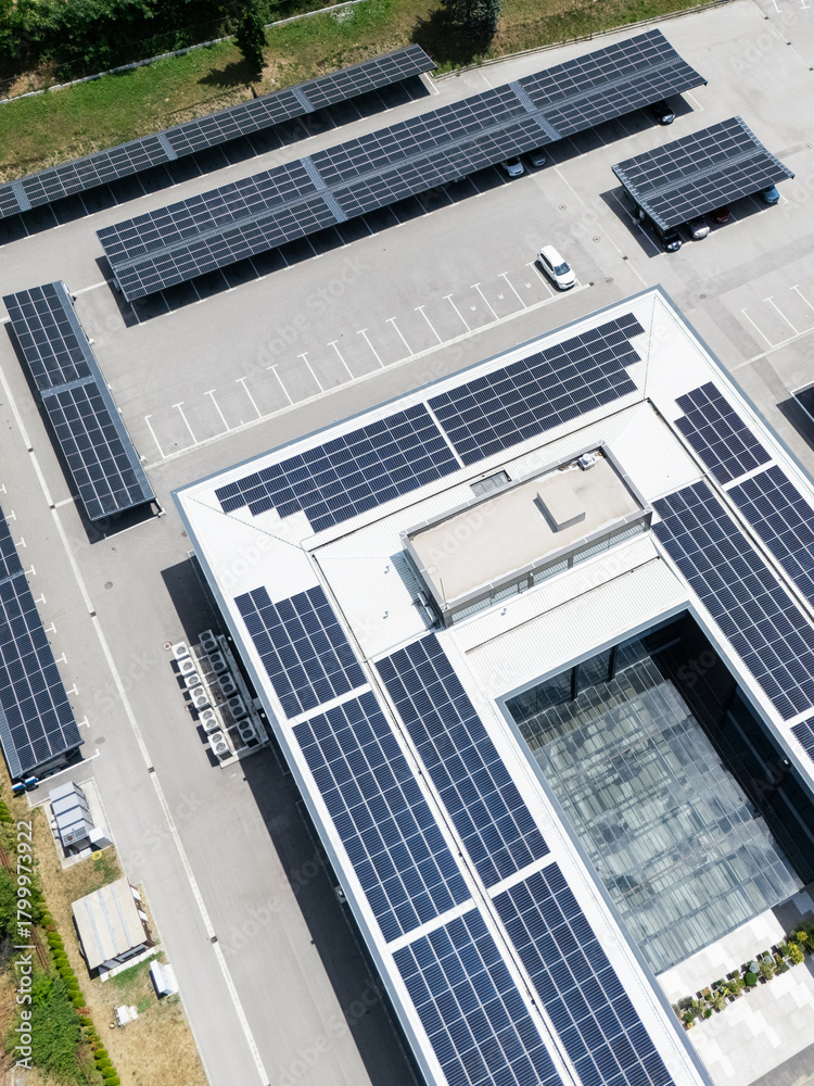 Obraz premium Aerial view of building with solar panels on a roof and parking space with solar canopies