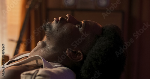 A tired man rests his head comfortably on the couch headrest, eyes closed, enjoying a peaceful nap after work in a quiet room, surrounded by calm and evening silence.