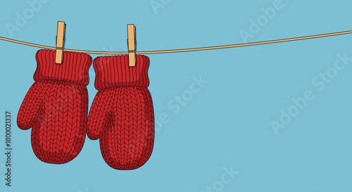 Pair of red knitted mittens hanging on a clothesline against a light blue background copy space