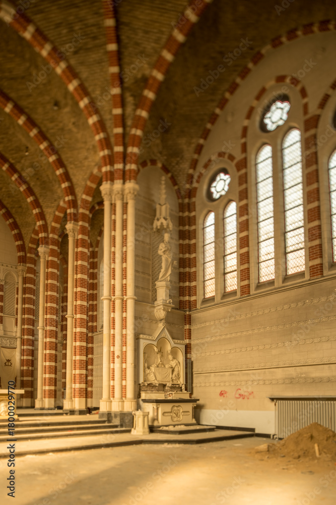 Fototapeta premium Sunlit abandoned church interior with striped brick arches, ornate altar and stained glass